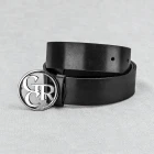 Zwinięty czarny pasek ze skóry z zaokrągloną końcówką, okrągłą srebrną klamrą z monogramem na szarej tkaninie.